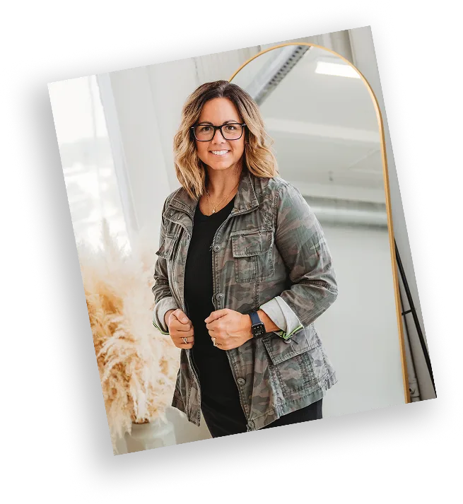 Natasha Roberson smiling in a camo utility jacket, standing in front of a mirror and pampas grass in a modern studio