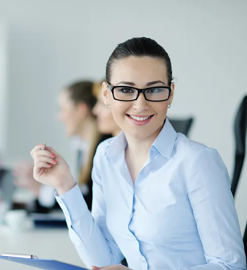 Confident businesswoman smiling with arms crossed, with team members blurred in the background, representing leadership and success.
