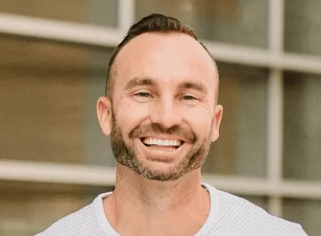 Friendly man with a trimmed beard smiling outdoors in front of a building.