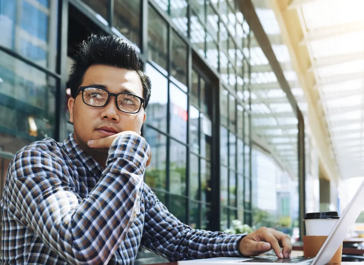 Man thinking while working on laptop in a modern workspace