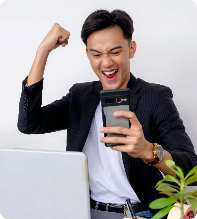 Man celebrating success while using phone and working on laptop