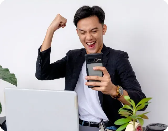Man celebrating success while using phone and working on laptop