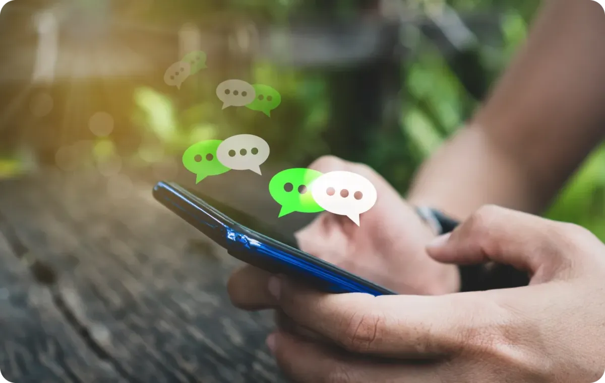 Close-up of a person holding a smartphone outdoors with floating chat message icons above the screen