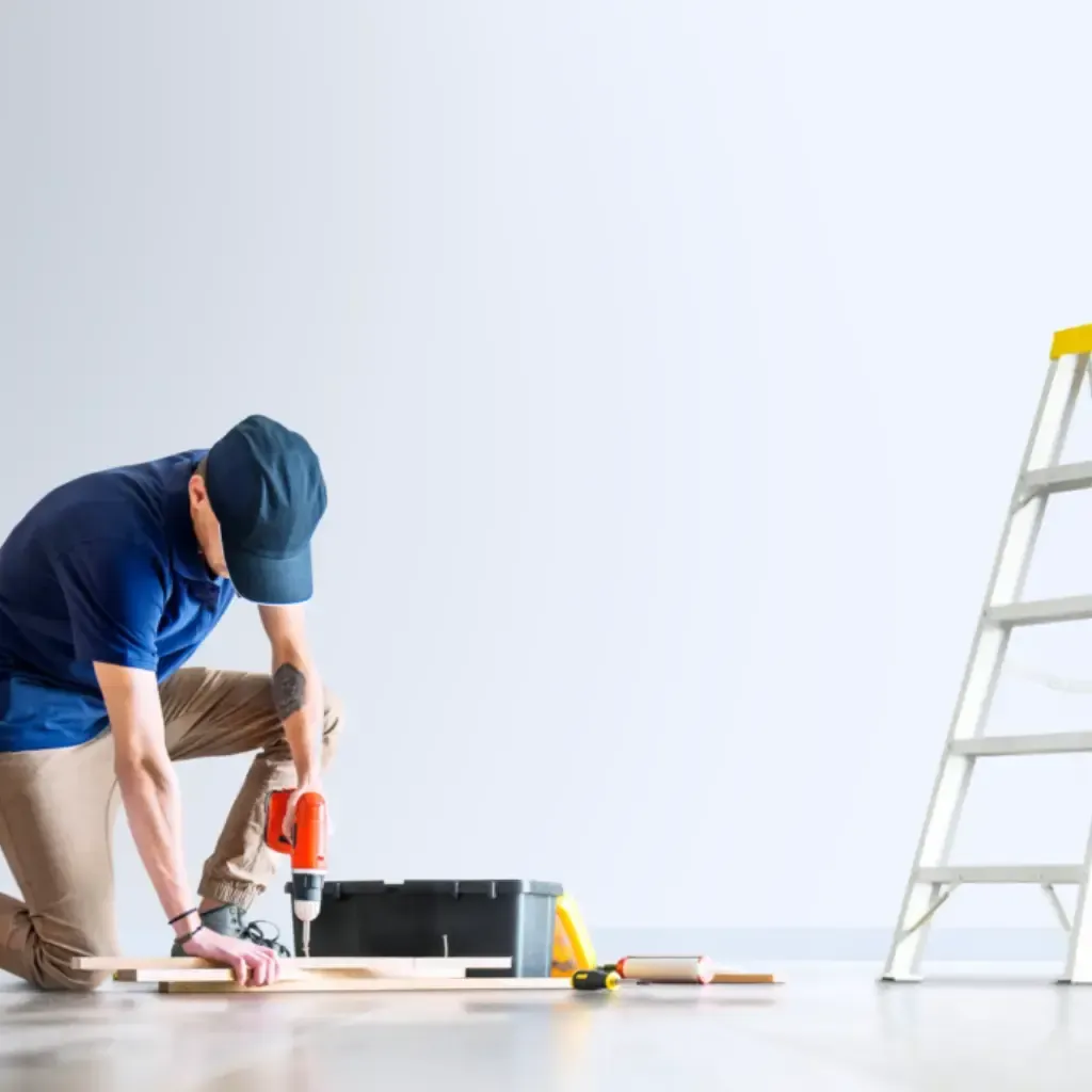 Carpenter using a power drill besides a ladder during indoor carpentry work, construction, and maintenance service.