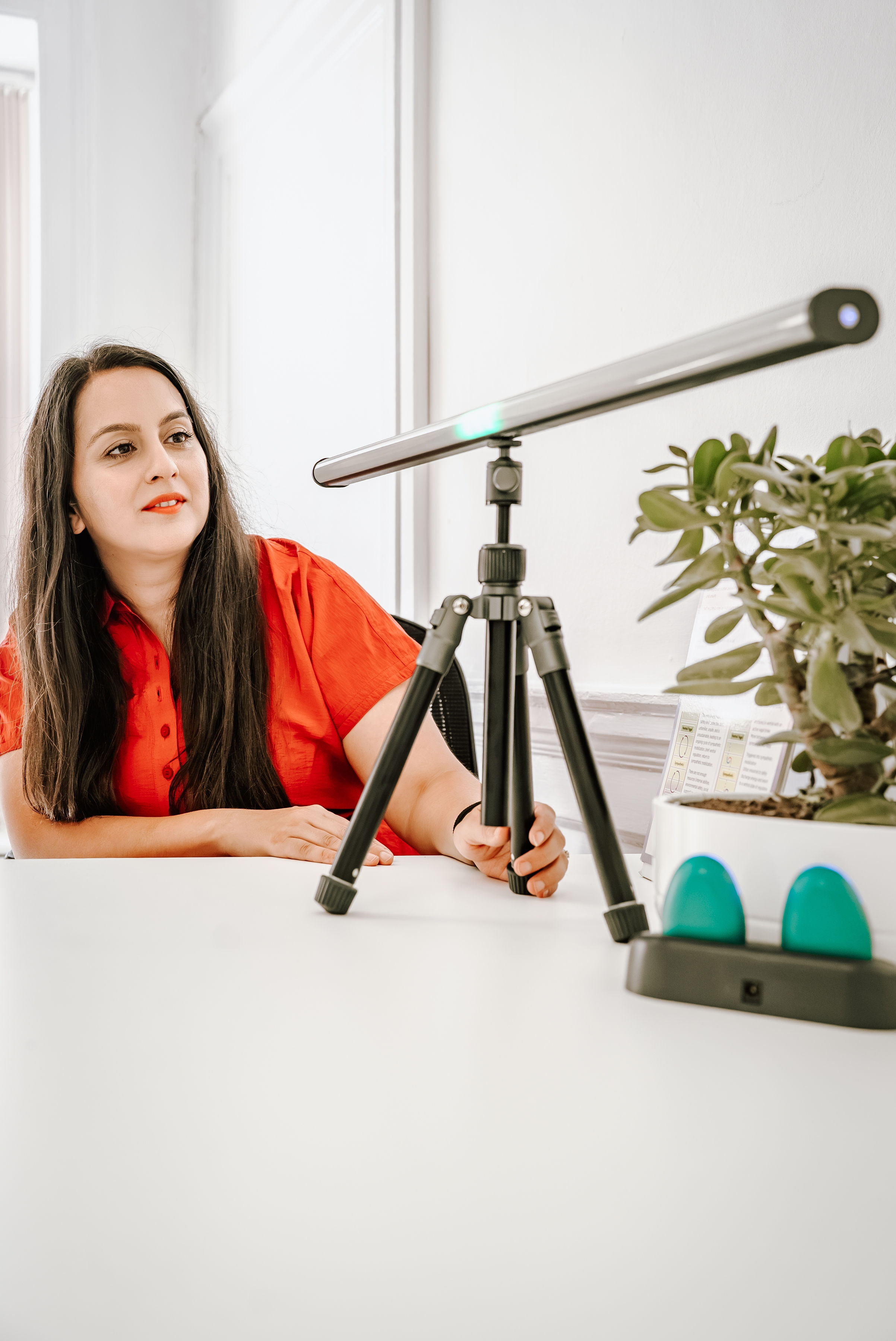 Dr Sara Schamborg seated beside an EMDR light bar on a tripod, with green handheld tactile pulsers on the desk, in a bright Bristol therapy room