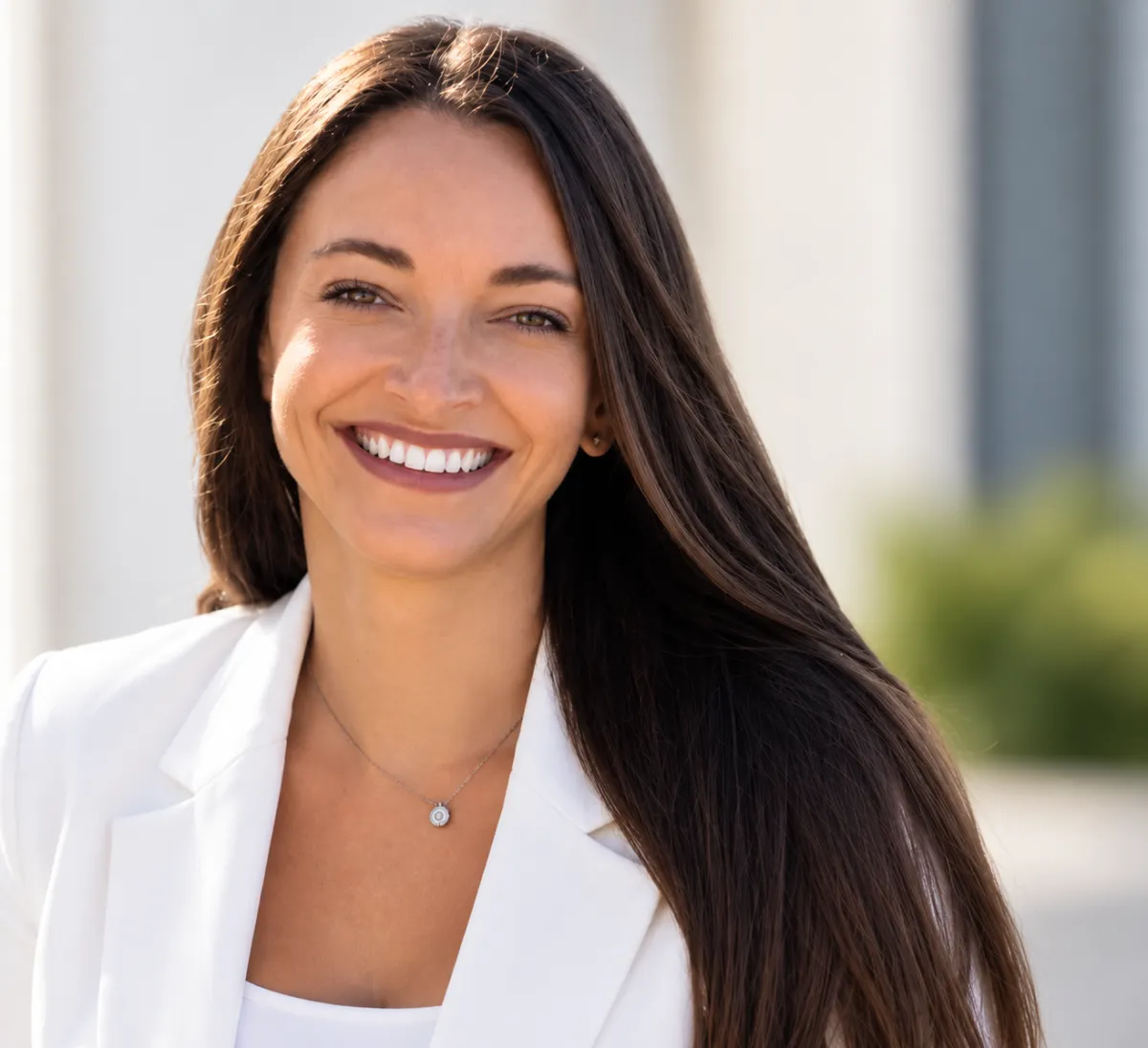 Portrait of a smiling woman in a dark blazer against a blurred indoor background.