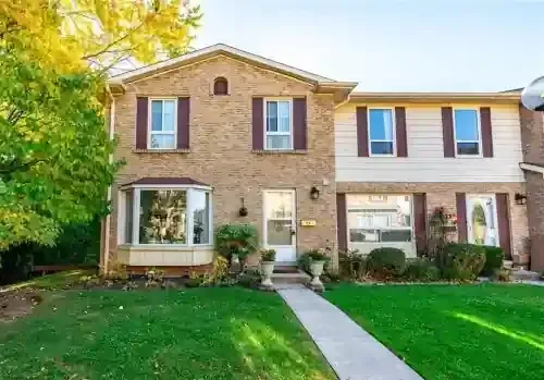 Two-story brick residential home with bay window, landscaped front yard, and walkway leading to entrance.