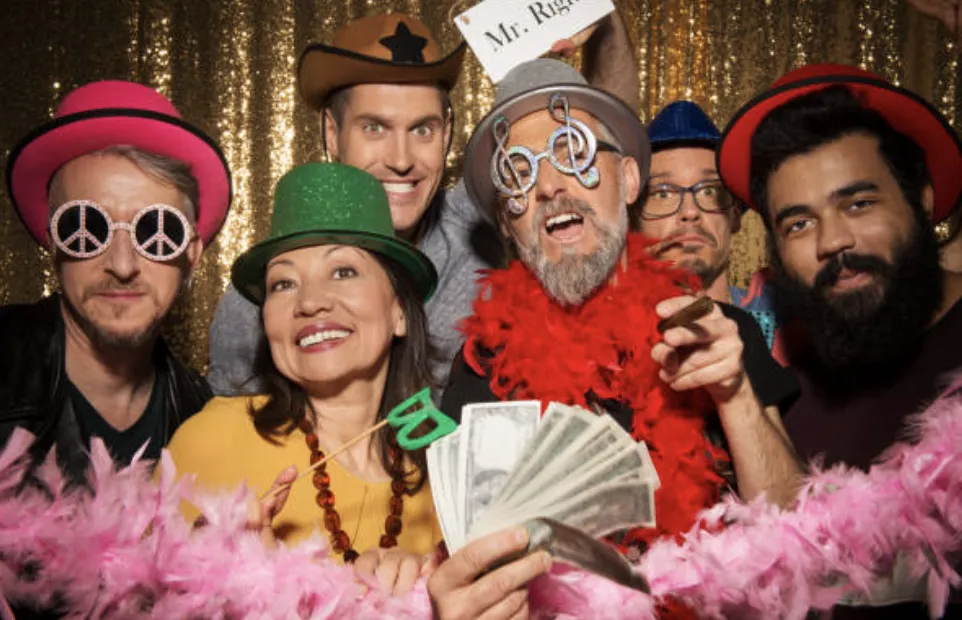 A group of guests dressed in funky hats and costumes, striking bold poses with silly props in a high-energy photo booth setting, ideal for corporate parties and wedding receptions in San Antonio, Austin, and College Station.