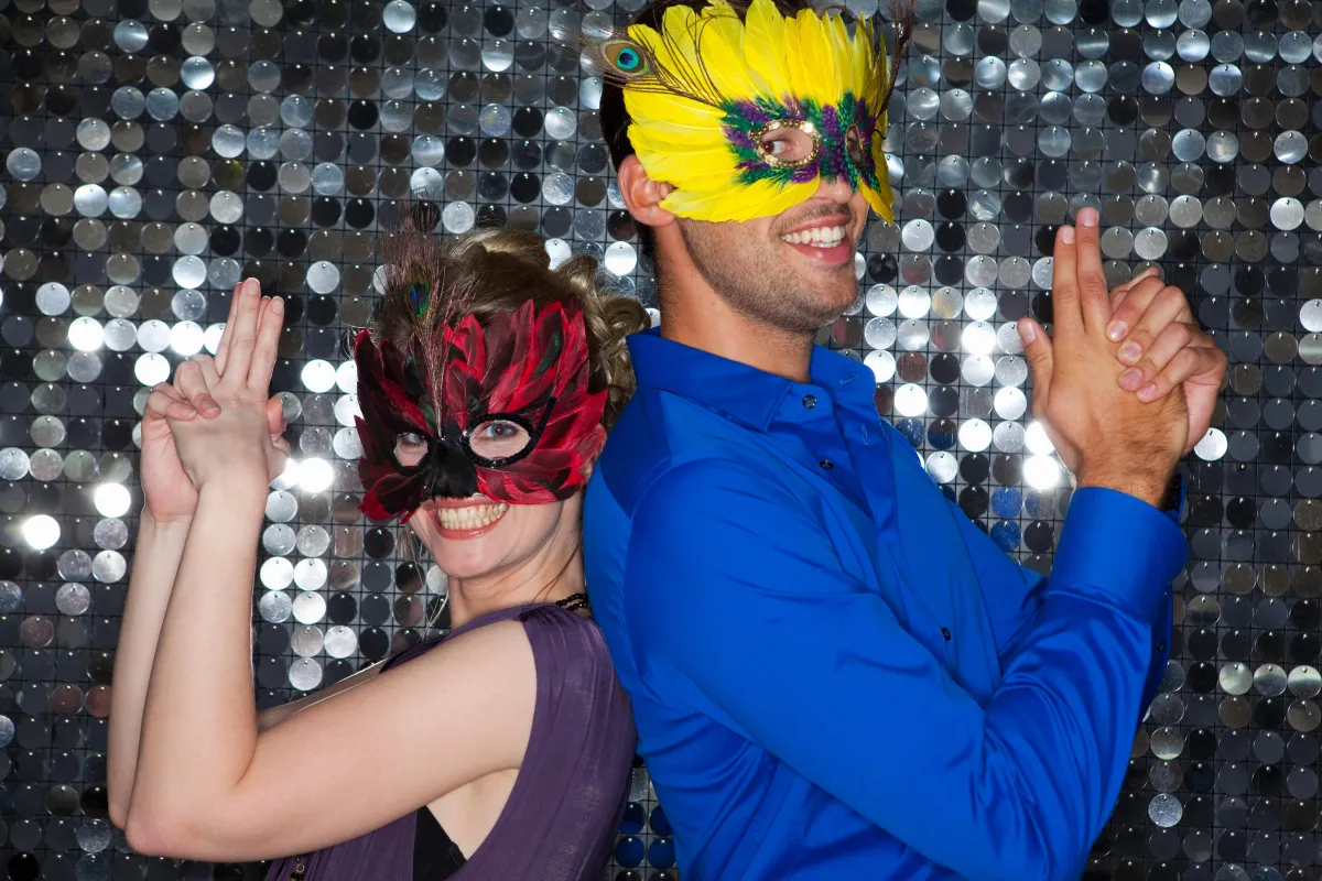 Fun and lively photo booth moment at an Austin wedding, featuring guests in vibrant masquerade masks posing against a sparkling sequin backdrop.