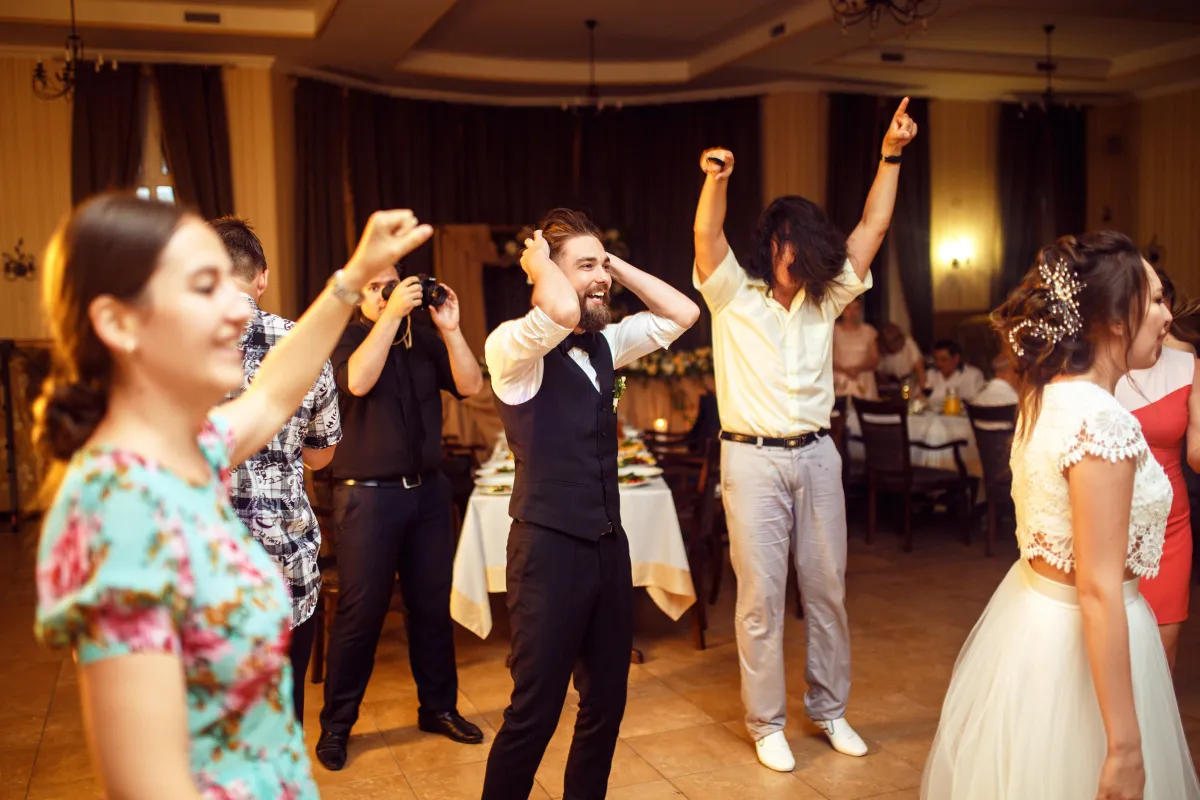 Wedding guests cheer and celebrate on the dance floor, creating a high-energy reception atmosphere with great DJ music.