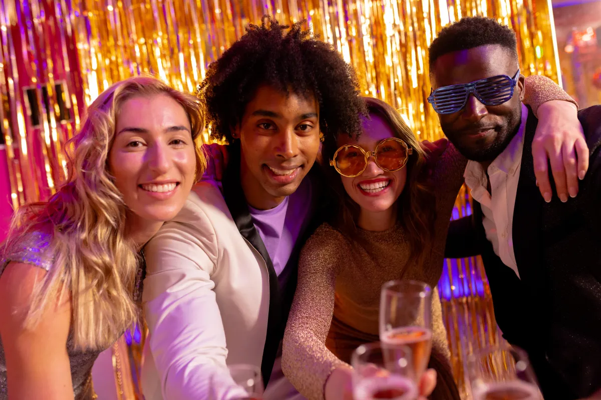 Group of friends celebrating at a wedding photo booth with champagne and fun props, hosted by Dynamic Celebrations.