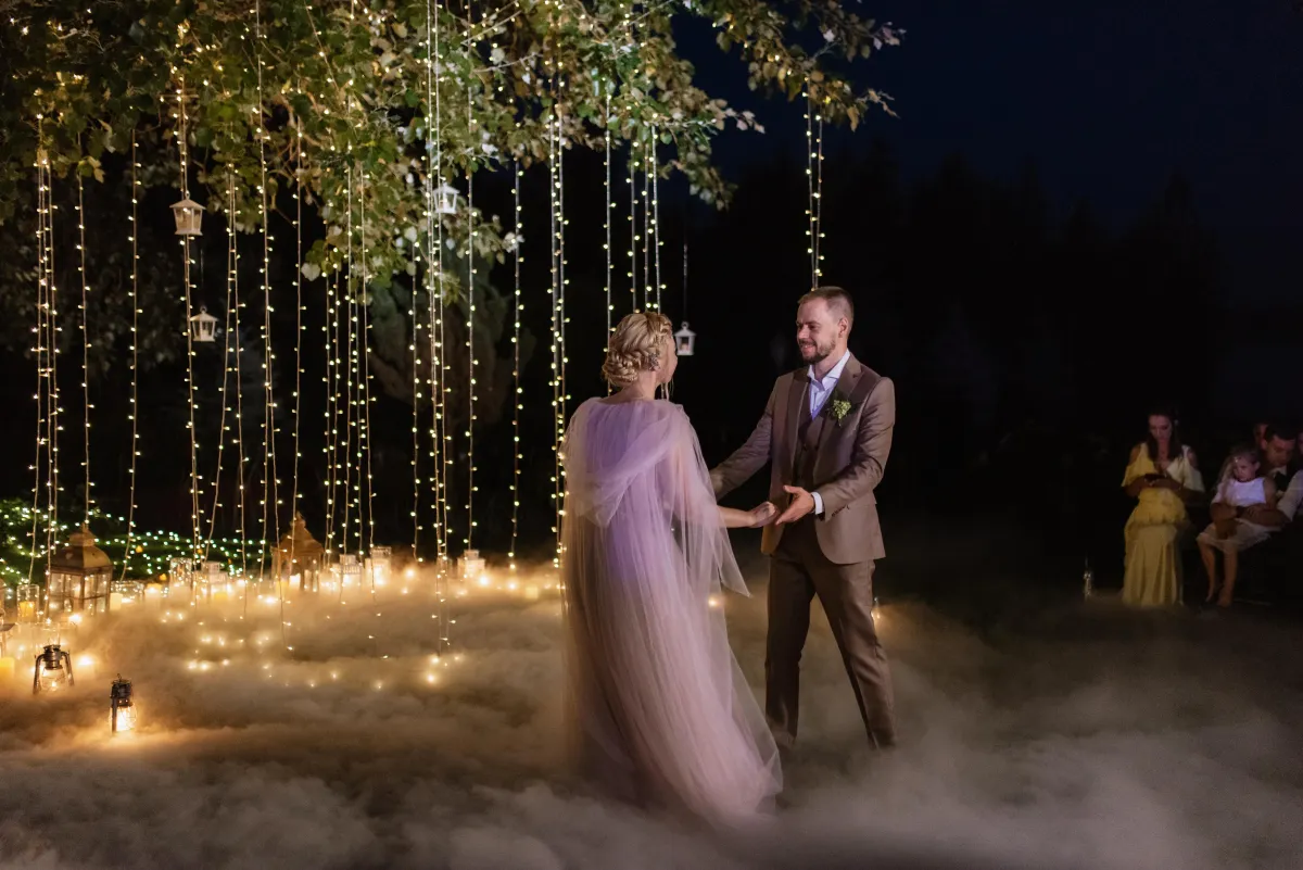 Enchanting outdoor wedding first dance in San Antonio, featuring romantic string lights, fog effects, and a beautifully dressed bride and groom.