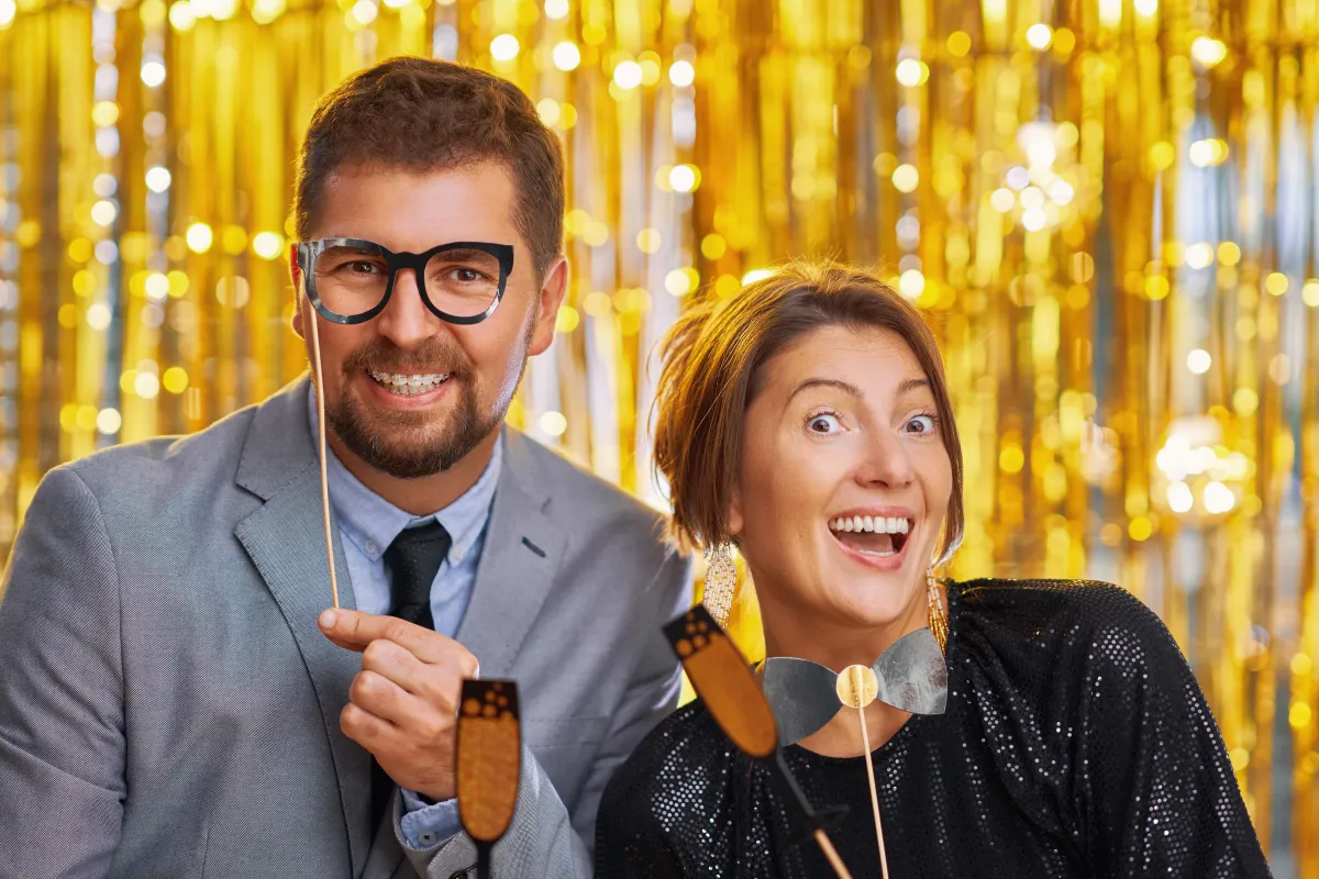 Fun wedding photo booth in San Antonio with guests posing against a gold backdrop, holding playful props and celebrating in style.