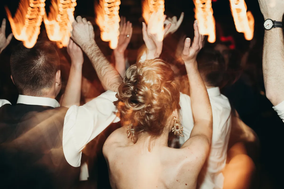 Bride and wedding guests dancing at a lively San Antonio wedding reception, celebrating with hands in the air and warm golden lights setting the mood.