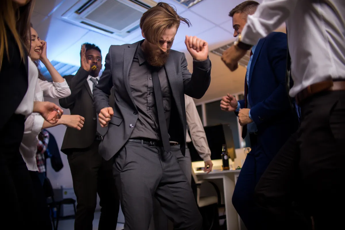 Business professionals dancing at an office party, dressed in suits and celebrating in a lively corporate event setting.