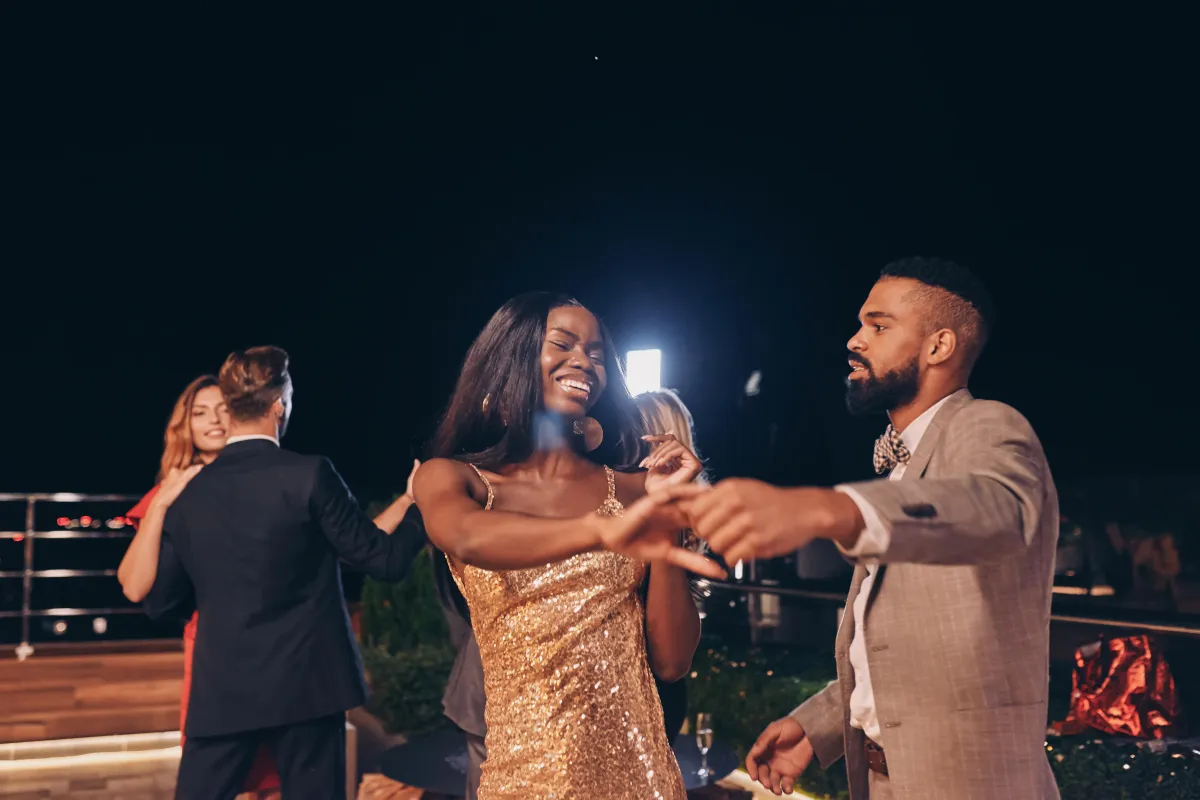 A couple dressed in gold and black dancing at an outdoor evening party, capturing a glamorous 360 moment in a scenic event setting with professional photo booth lighting.