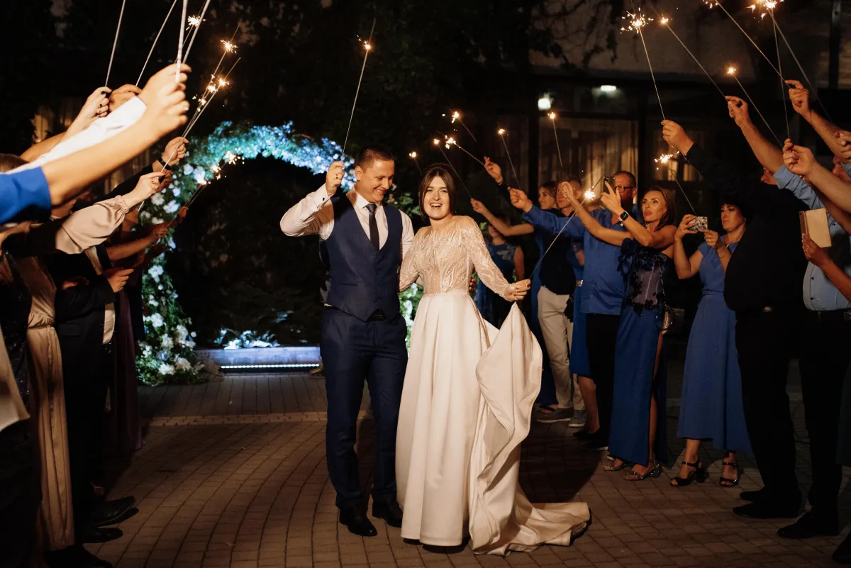 A joyful bride and groom walk through a tunnel of guests holding sparklers, creating a breathtaking wedding exit moment.