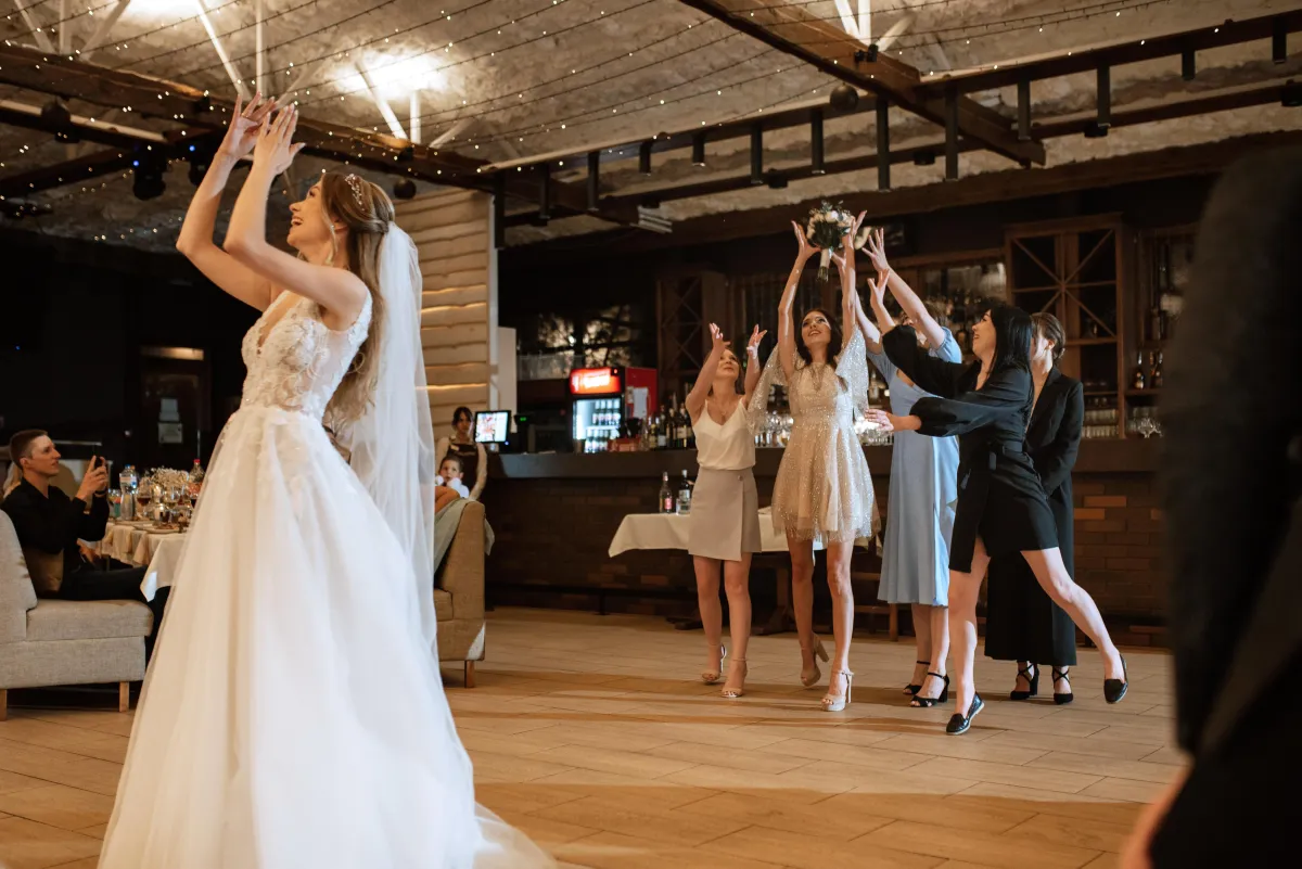 Bride tossing her bouquet in a stylish wedding venue with excited guests - Wedding DJs and photo booths in San Antonio.