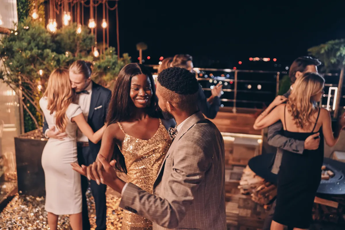 Elegantly dressed guests twirl under the starlit sky, celebrating a magical wedding night on an illuminated outdoor terrace.