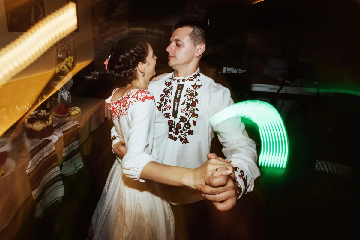 A newlywed couple in beautifully embroidered traditional wedding attire shares an intimate first dance, enhanced by professional DJ lighting and a curated wedding playlist.