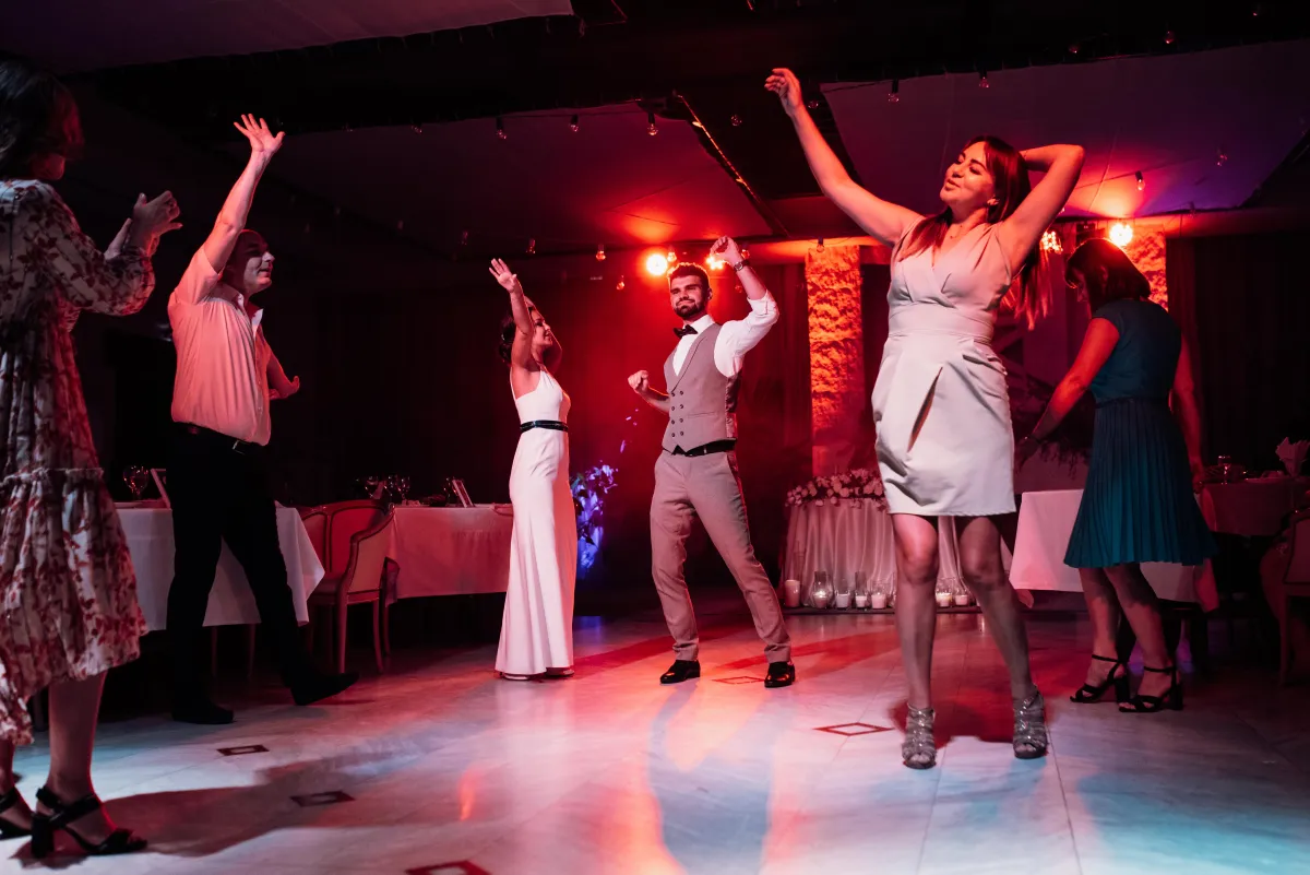 Guests celebrate on the dance floor, dancing under colorful DJ lighting, creating an unforgettable wedding reception experience.