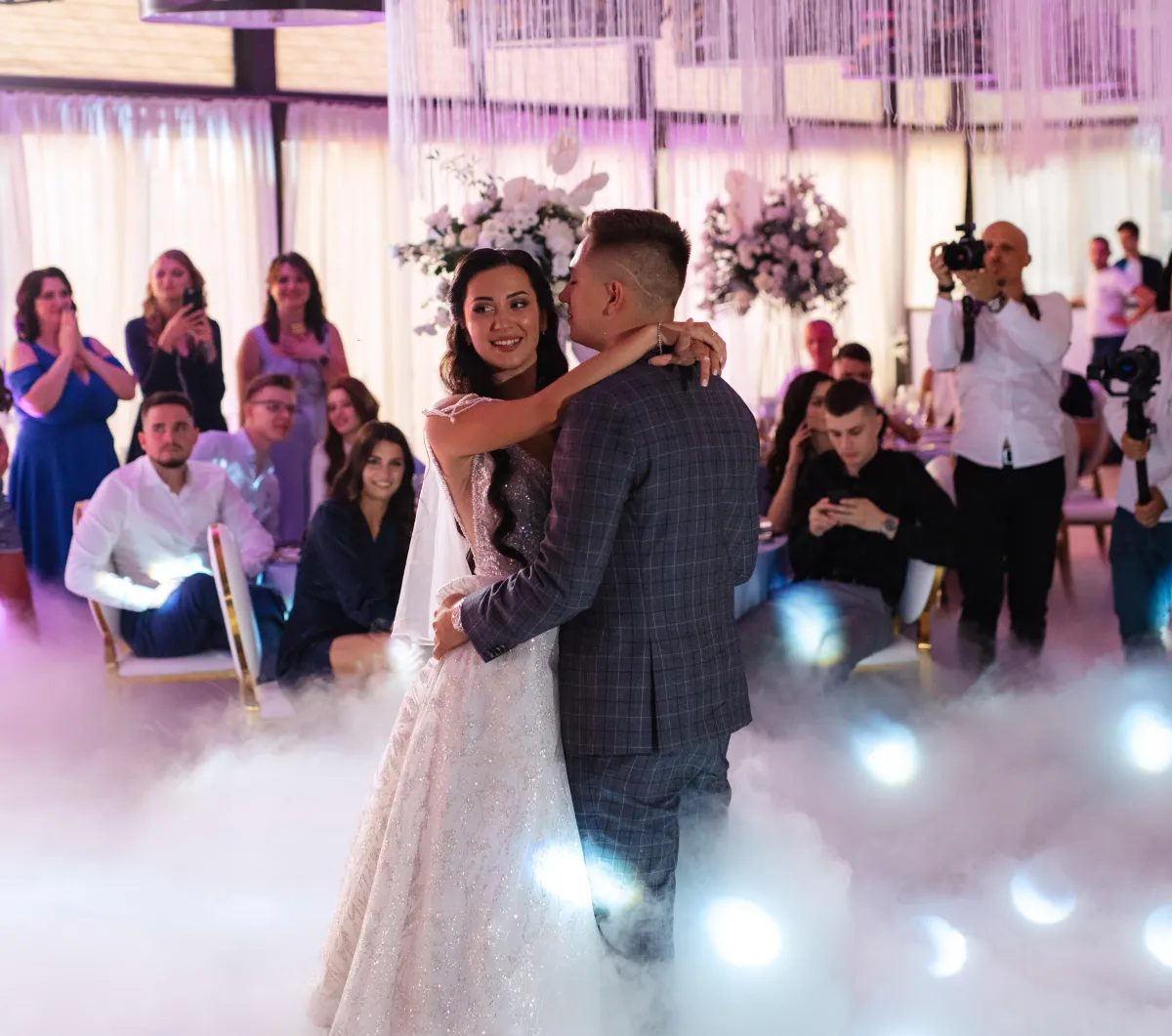 Bride and groom share their romantic first dance on a dreamy cloud-like dance floor at a luxurious Austin, Texas wedding reception, surrounded by guests and photographers.