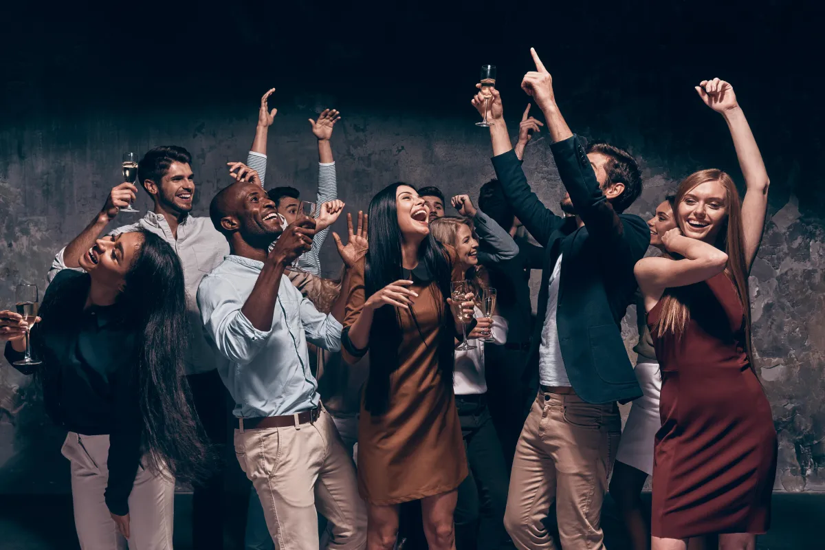 "A stylish group of diverse young professionals dancing and celebrating with champagne at a lively party, dressed in semi-formal attire with energetic expressions.