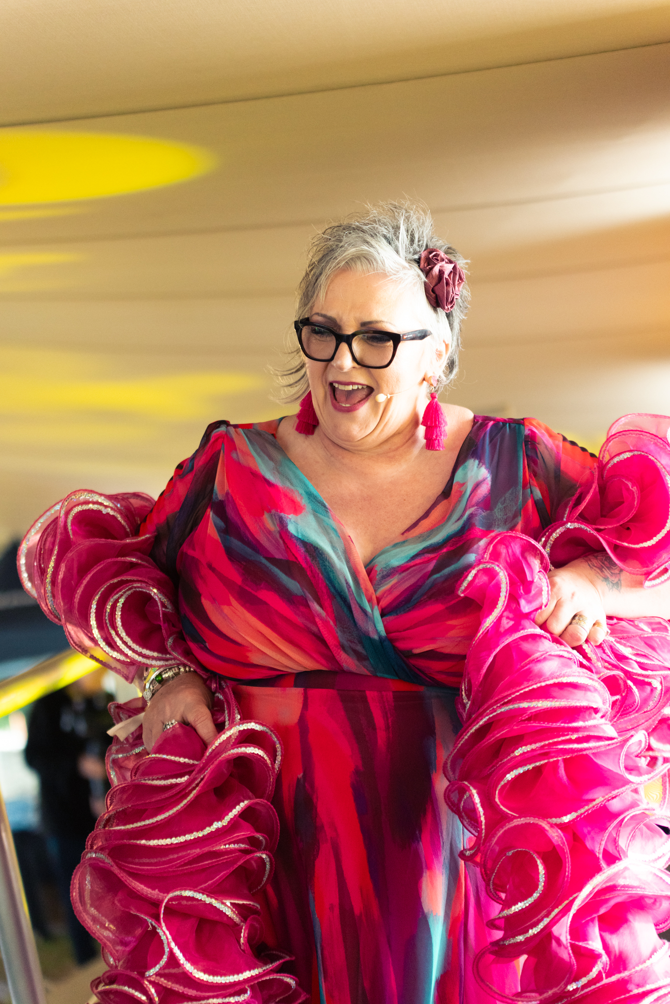 Lisa Newport laughing in a bright pink and red ruffled dress with tassel earrings and a flower in her hair