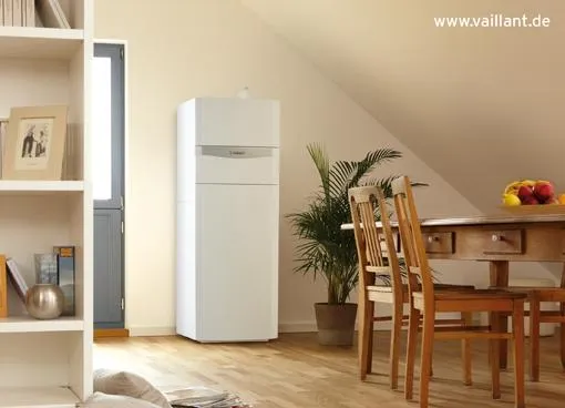 Vaillant Heizsystem in einem modernen, gemütlichen Wohnbereich unter dem Dach. Das kompakte Heizgerät steht dezent in einer Ecke des Raums neben einem Esstisch aus Holz, umgeben von Zimmerpflanzen und natürlichem Licht. Das stilvolle Design fügt sich harmonisch in die helle und freundliche Raumgestaltung ein.