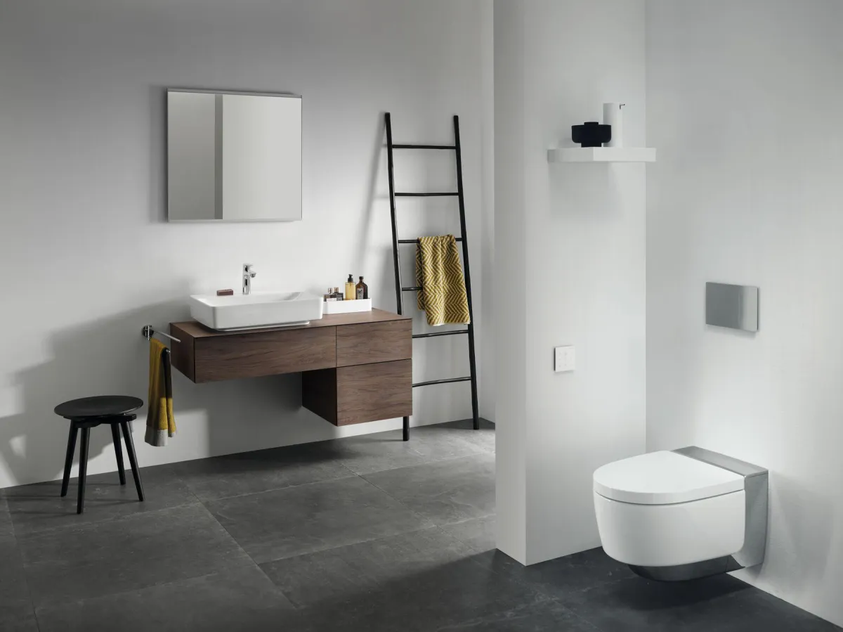 Modernes Badezimmer mit minimalistischer Einrichtung. Ein wandhängendes WC und ein schwebender Waschtisch mit Holzschubladen ergänzen das klare Design. Schwarze Akzente, wie ein Hocker und eine Handtuchleiter, setzen stilvolle Kontraste zu den hellen Wänden und dunklen Bodenfliesen. Der große Spiegel und die dezenten Accessoires betonen die Eleganz und Schlichtheit des Raumes.