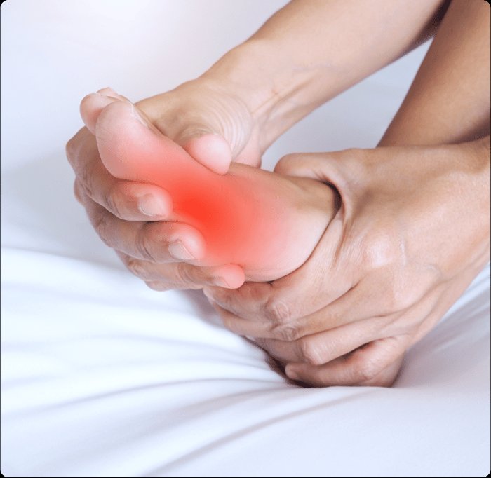 Woman in athletic gear sitting on the ground outdoors, grabbing her lower leg/ankle in pain.
