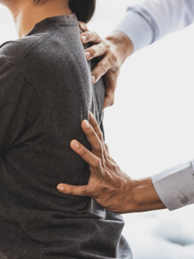 Mid-section view of a person wearing a grey shirt, holding their lower back as if experiencing back pain