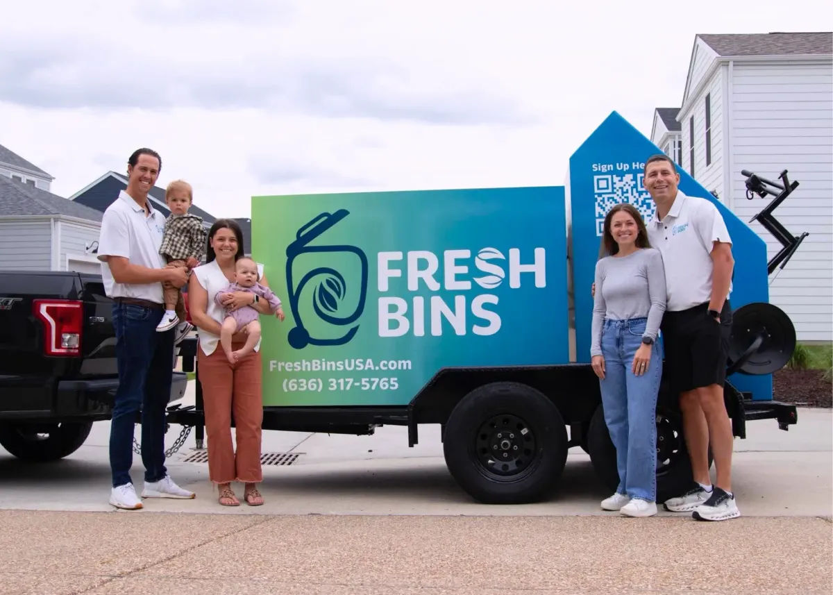 Fresh Bins trash bin cleaning service team standing with families in front of branded trailer in suburban neighborhood.