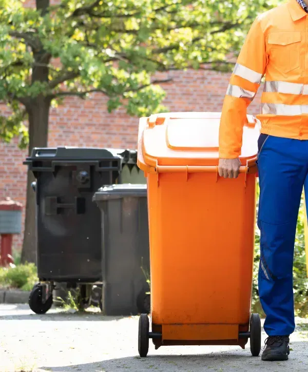 Sanitation worker pulling an orange garbage bin on a residential street