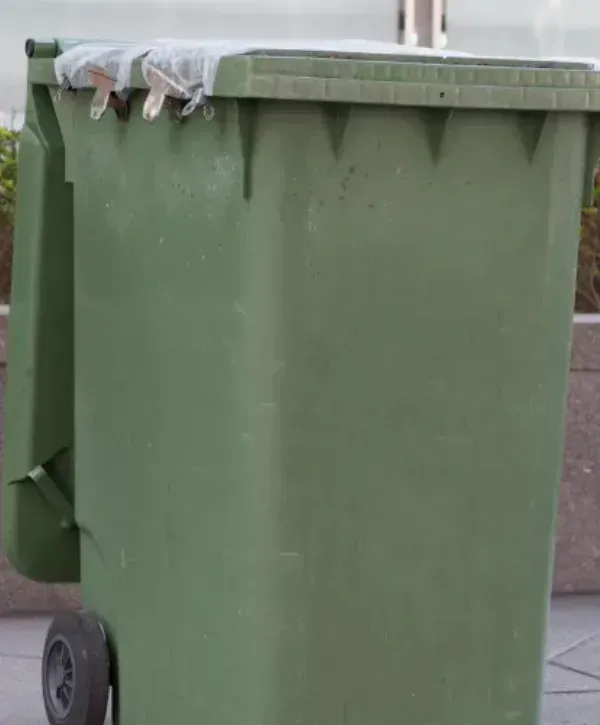 Large green trash bin placed outdoors on a paved area.