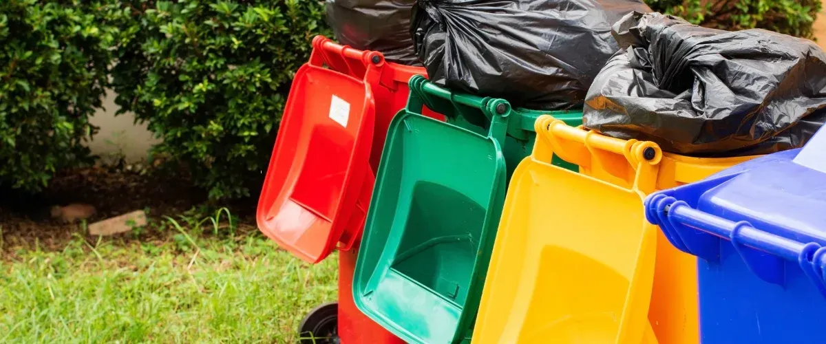 Colorful outdoor trash bins with open lids and garbage bags on top, ready for cleaning.