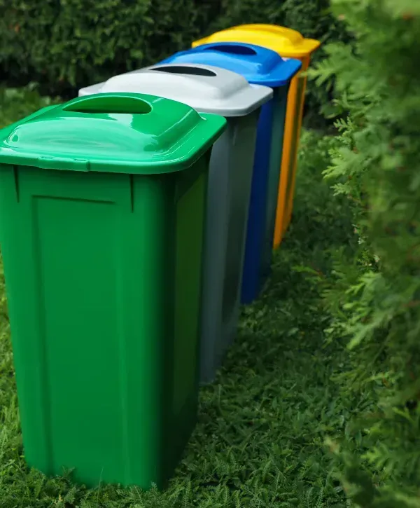 Row of green, gray, blue, and yellow recycling bins placed neatly in a garden for waste separation.