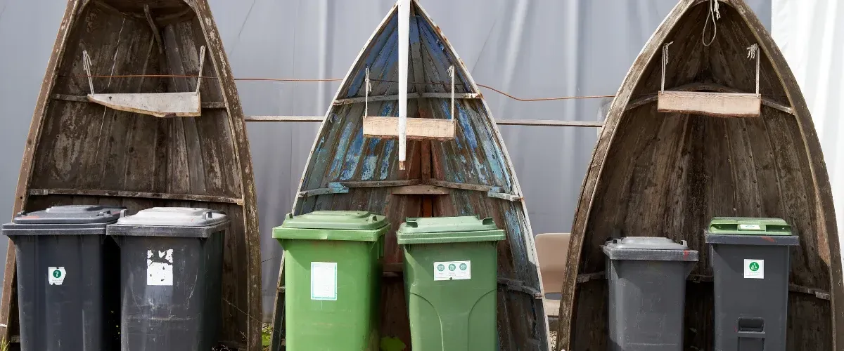 Green and black garbage bins placed in front of wooden sheds during waste management service