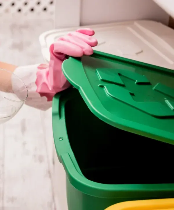 Person wearing pink gloves opening a green recycling bin lid indoors.