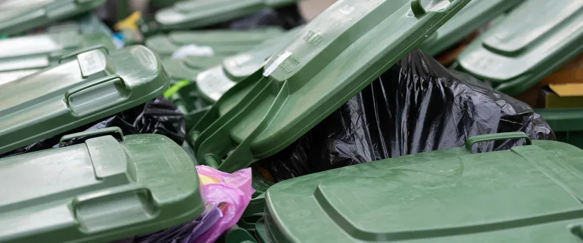 A close-up view of multiple green dumpster lids and black trash bags overflowing with waste.