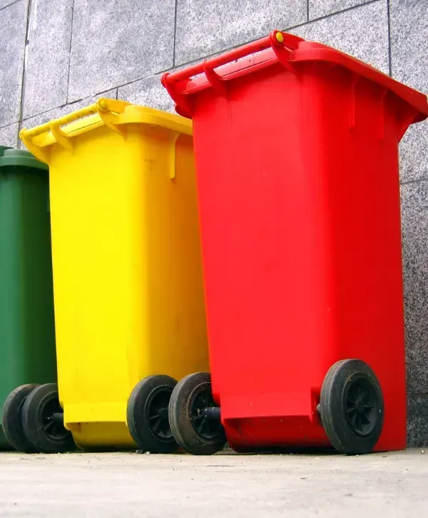 Yellow and red trash bins lined up against a gray wall on a city sidewalk.