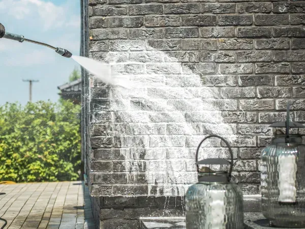 Close-up of pressure washing on a dark brick wall removing dirt and stains.