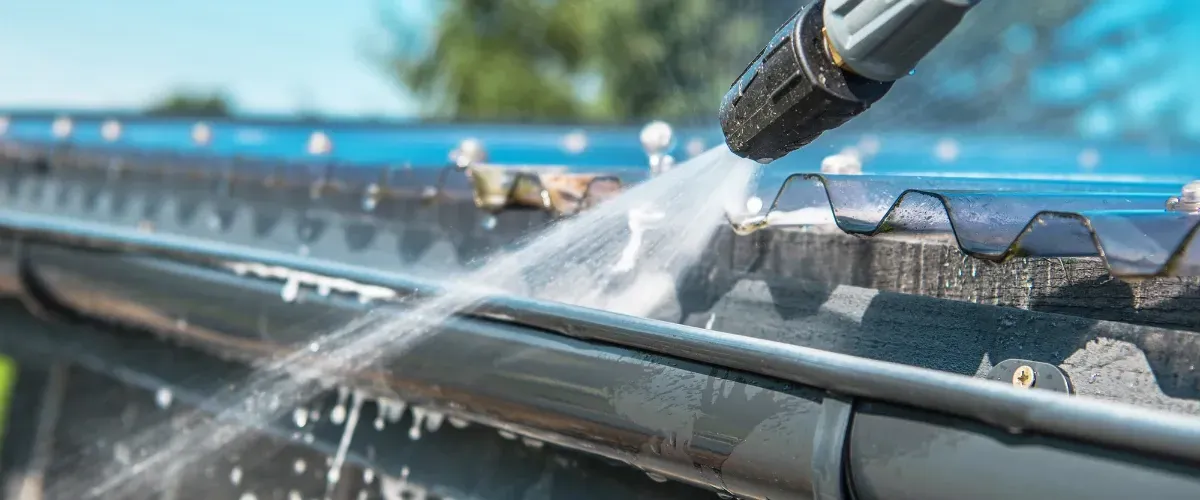 High-pressure washer cleaning residential roof gutter for maintenance and debris removal.