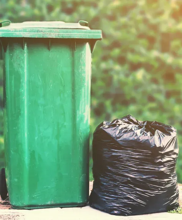 Green trash bin next to full black garbage bag