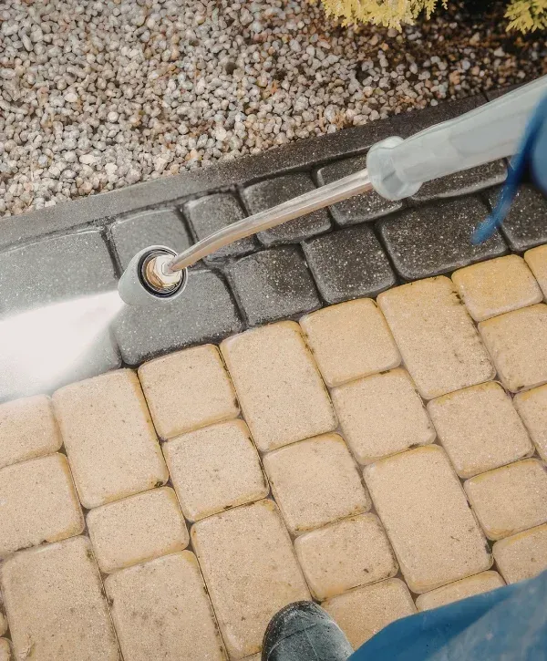 A pressure washer cleaning dirty paving stones, revealing cleaner, lighter-colored sections beneath.