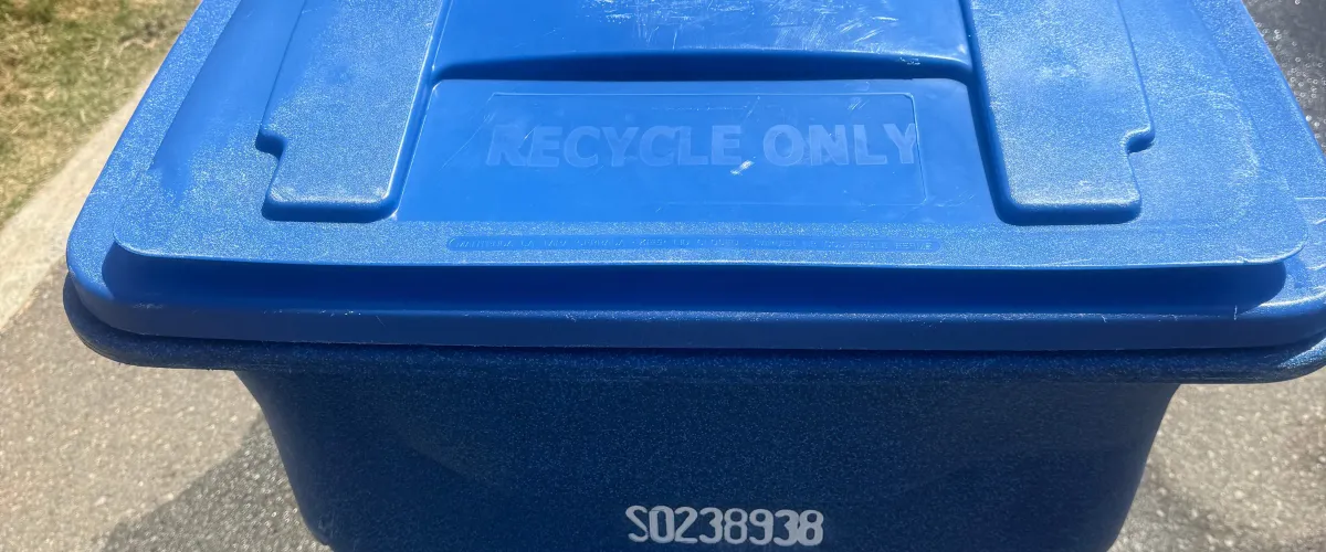 A close-up, slightly angled view of a blue recycling bin lid with 'RECYCLE ONLY' embossed on top and a serial number S0238938 visible.