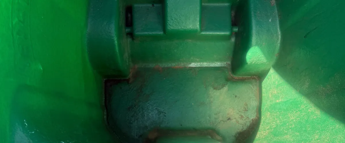 A close-up, top-down view of a dark green, weathered industrial surface with geometric shapes and subtle discoloration.
