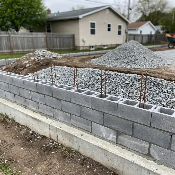 Partially built concrete block retaining wall with drainage gravel and rebar reinforcement in North Tonawanda, New York