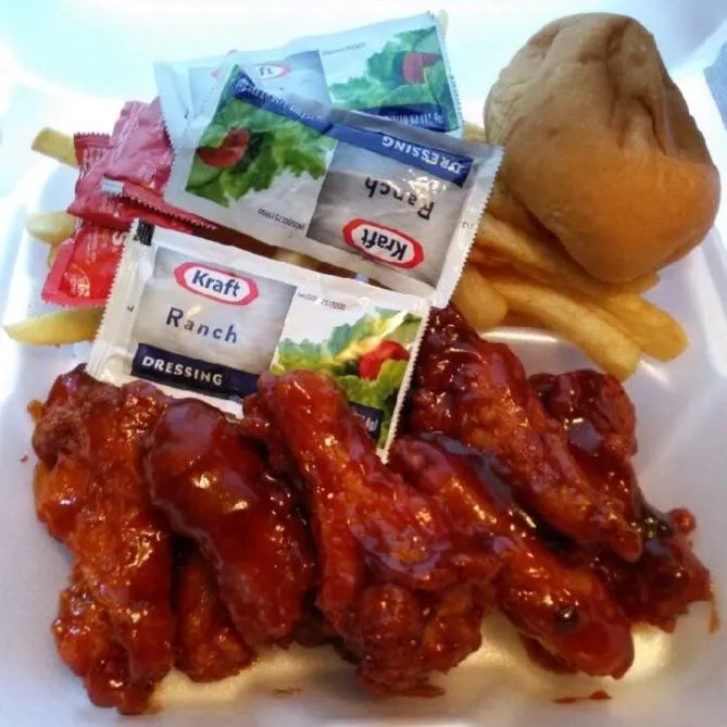 Photorealistic platter of crispy chicken wings tossed in a sticky hot sauce with a small cup of blue cheese dip.