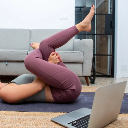 Person practicing yoga at home with a laptop and yoga mat